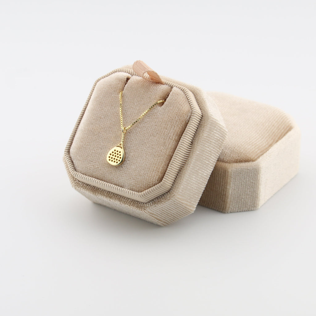 Beige jewelry box with a gold padel necklace on a light gray background