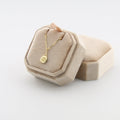 Beige jewelry box with a gold padel necklace on a light gray background
