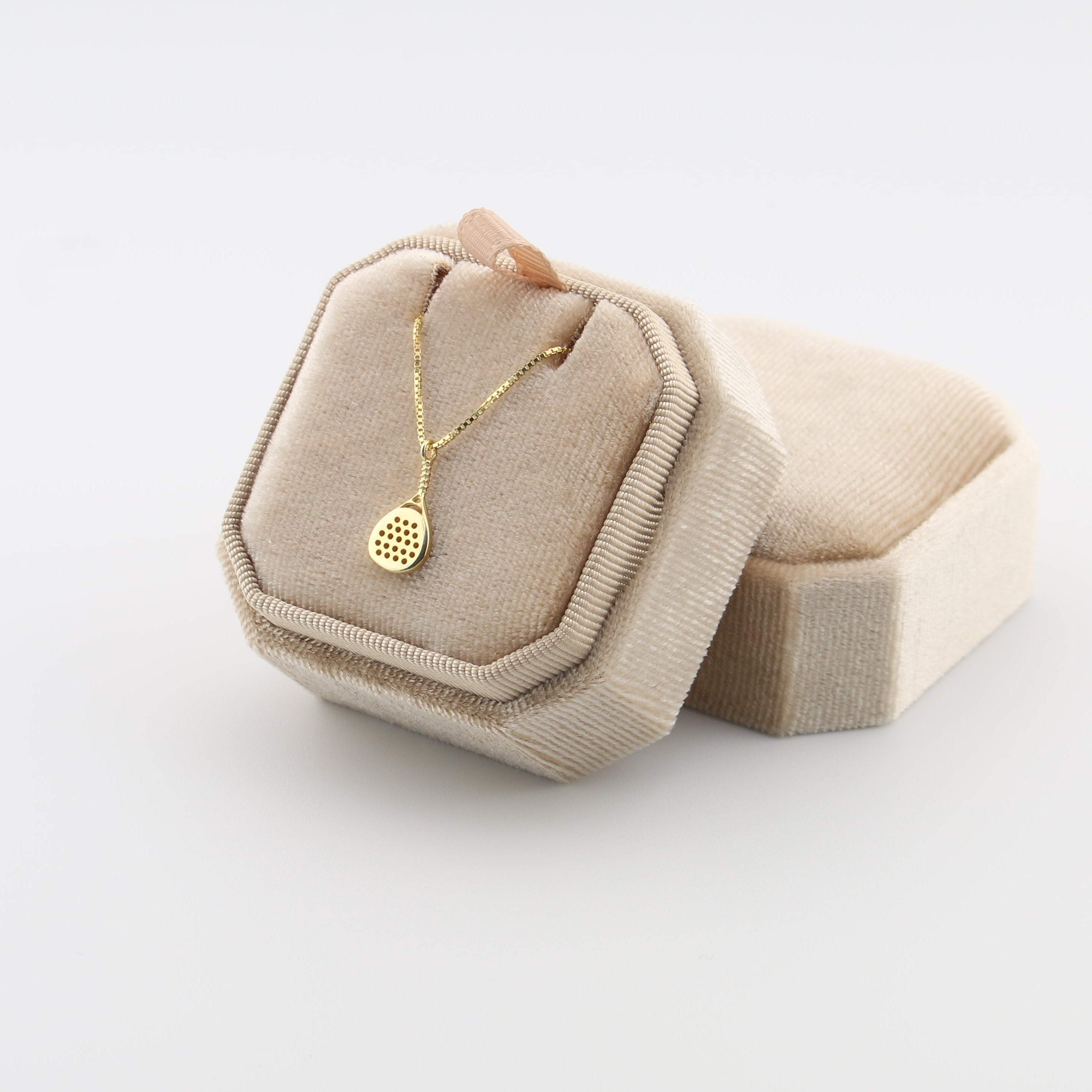 Beige jewelry box with a gold padel necklace on a light gray background