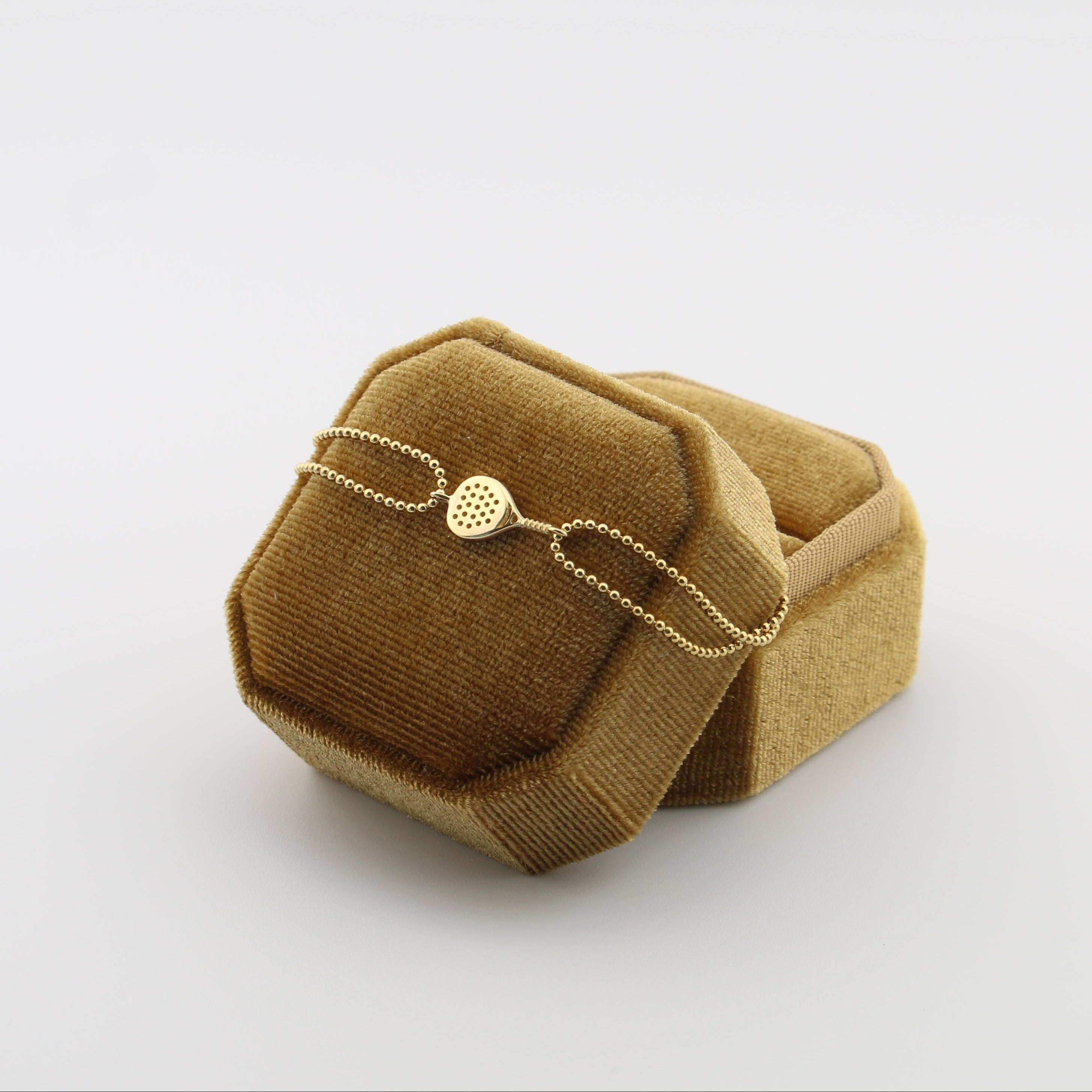 Gold padel bracelet on a brown velvet cushion against a white background