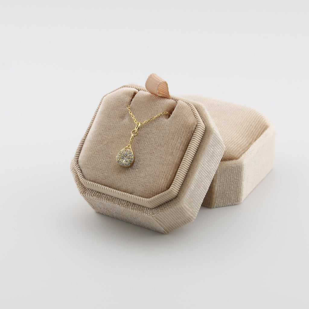 Rhinestone padel necklace with a pendant on a beige jewelry display box against a light gray background