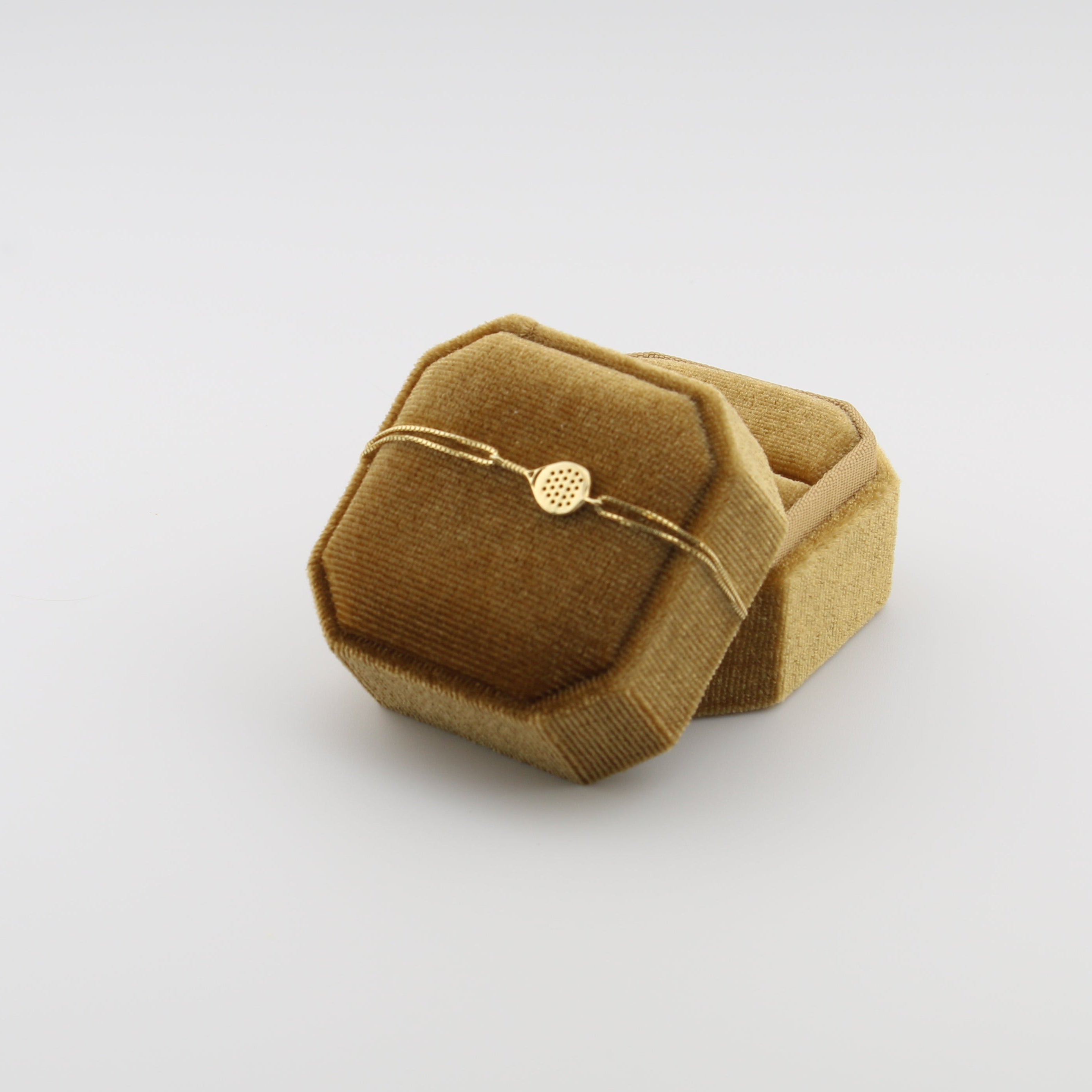 Gold padel bracelet on a brown velvet cushion against a white background