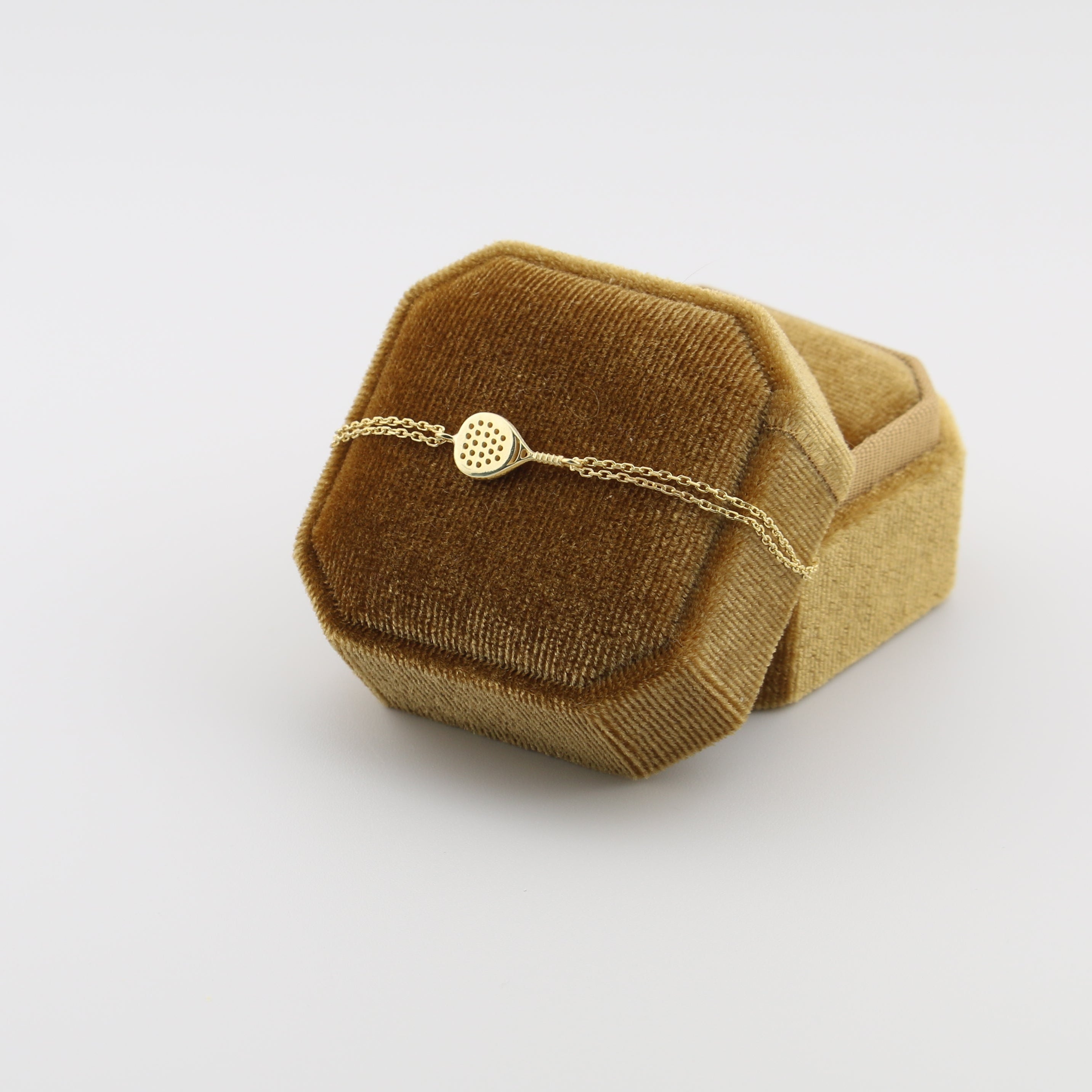 Gold padel bracelet on a brown velvet cushion against a white background