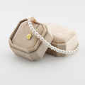 Pearl necklace with a gold padel pendant in a beige jewelry box on a light gray background