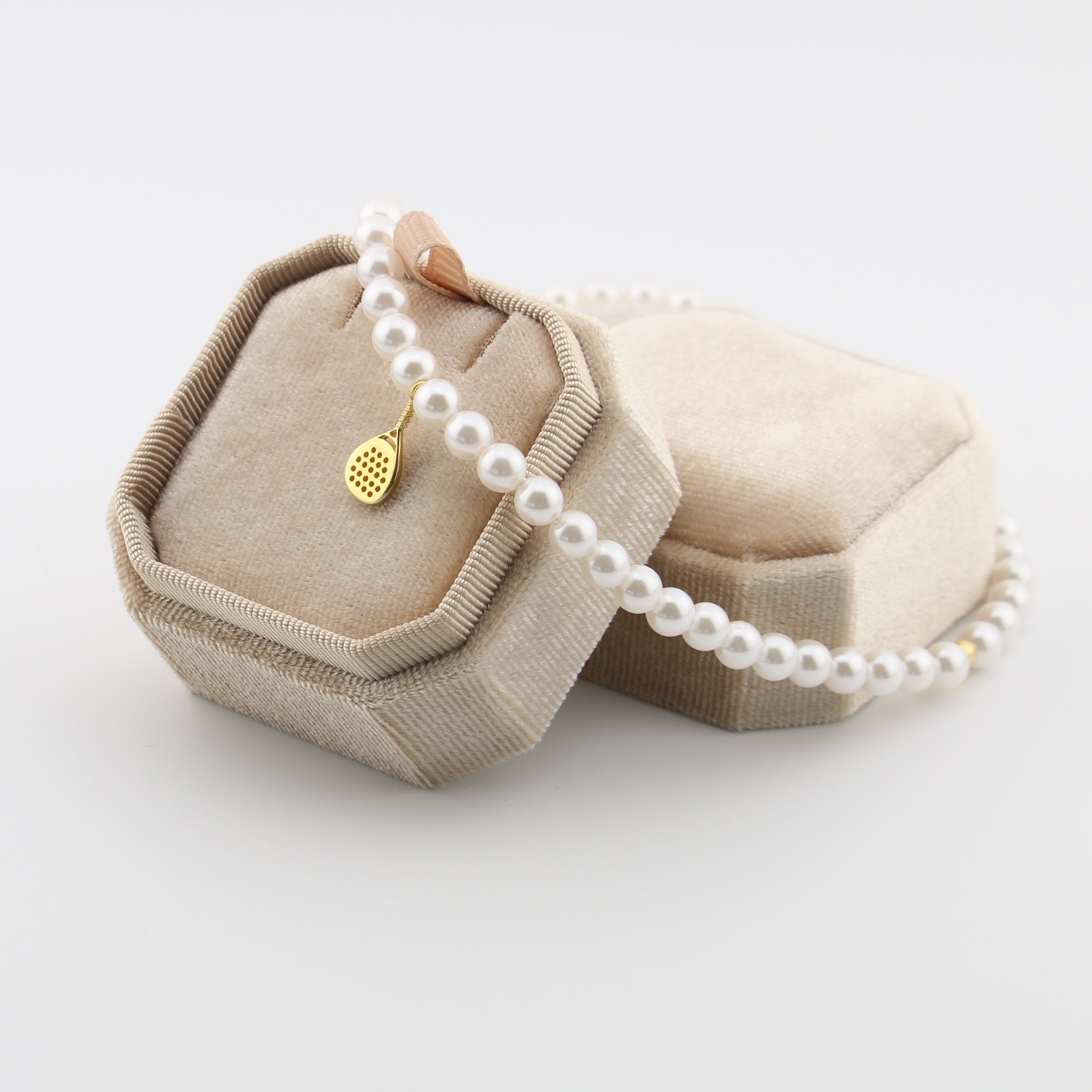 Pearl necklace with a gold padel pendant in a beige jewelry box on a light gray background