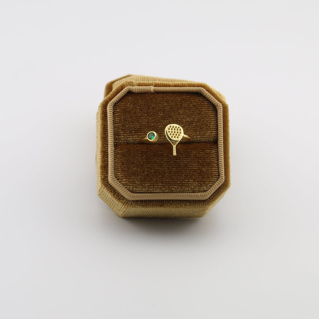 Gold padel  racket and ball brooch on a brown velvet cushion in a decorative box.