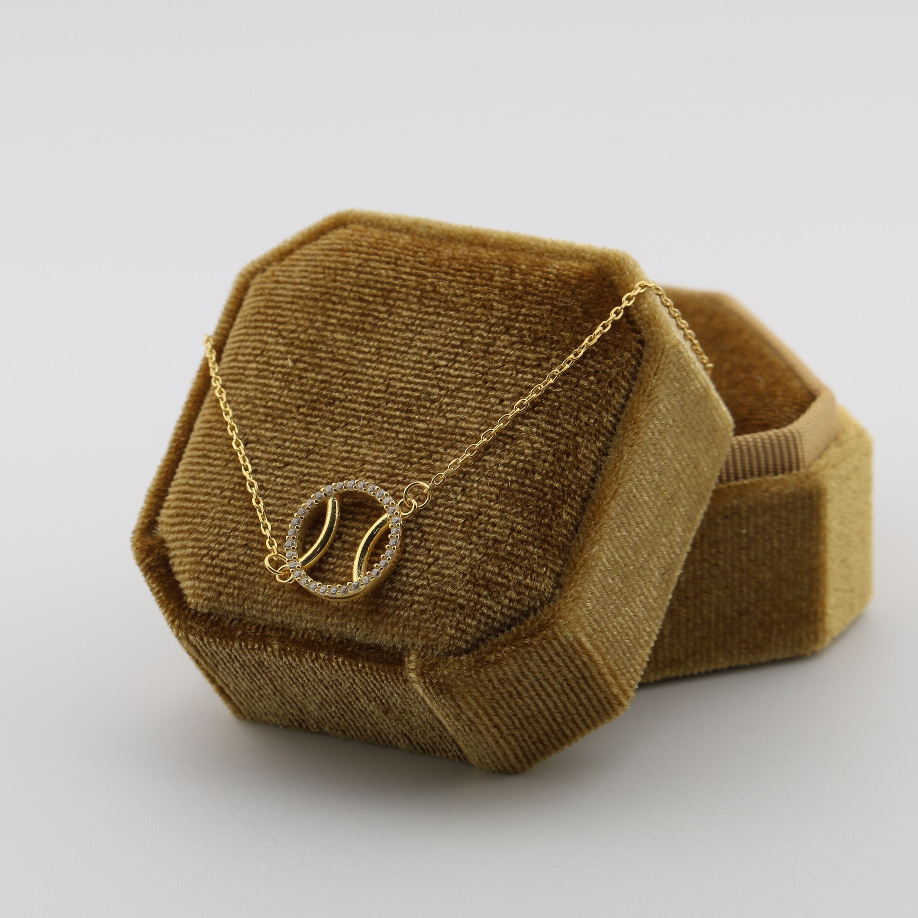 Brown geometric jewelry box with a padel ball necklace on a white background