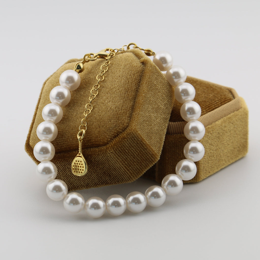 Pearl bracelet with gold clasp on a textured brown box against a light gray background