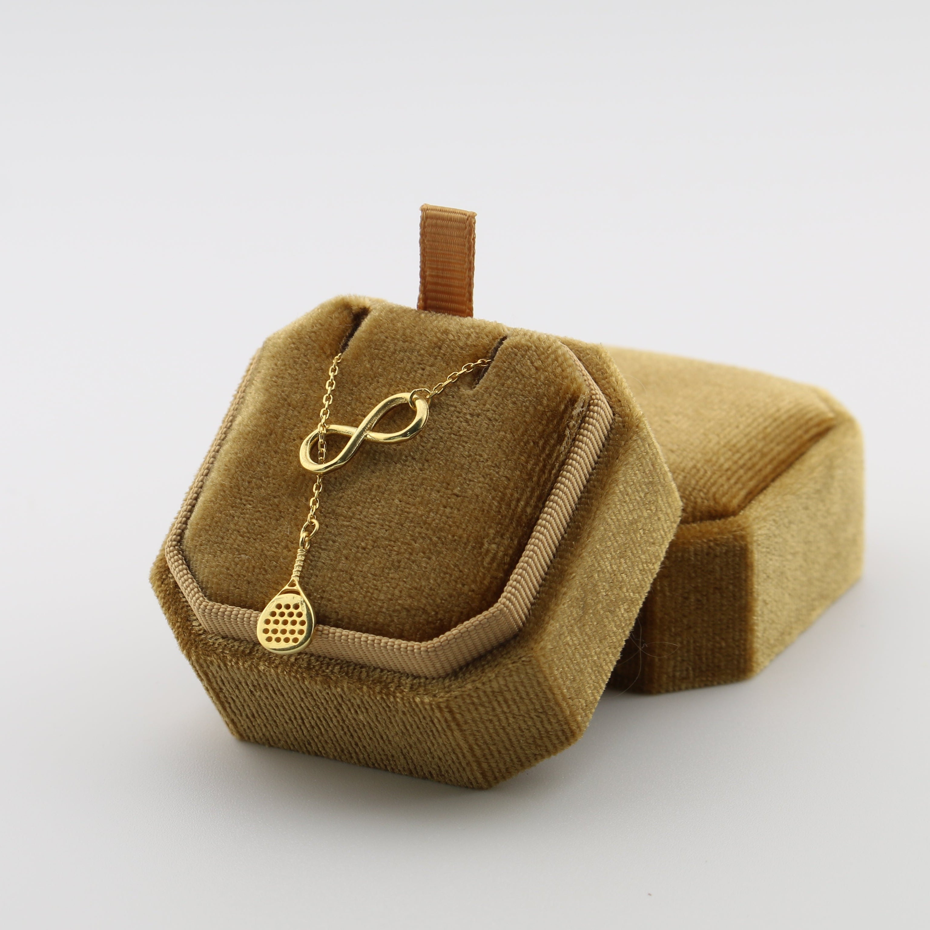 Gold necklace with an infinity symbol on a brown velvet stand against a white background